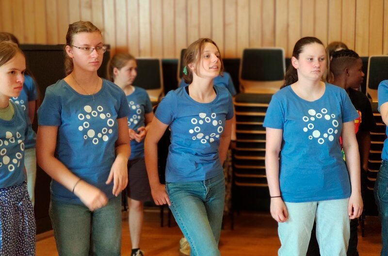 Zwei Jugendchöre, die „Vokalhelden“ aus Berlin und der „Ndlovu Youth Choir“ aus Johannesburg, treffen für einen gemeinsamen Auftritt aufeinander. Mittendrin die 14-Jährige Clara, für die Singen eine wichtige Rolle in ihrem Leben spielt. Sie freut sich auf die gemeinsame Zeit und den Auftritt mit dem Chor aus Johannesburg. Werden die beiden Chöre miteinander harmonieren? Clara mit den Vokalhelden beim Workshop. – Bild: rbb/​Matthias Eder
