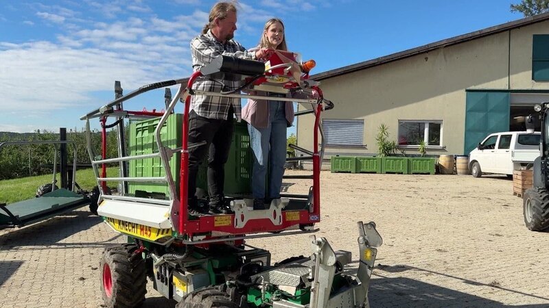 Obstbauer Wolfgang und Lena fahren auf einem Erntefahrzeug zur Apfelplantage. – Bild: ORF