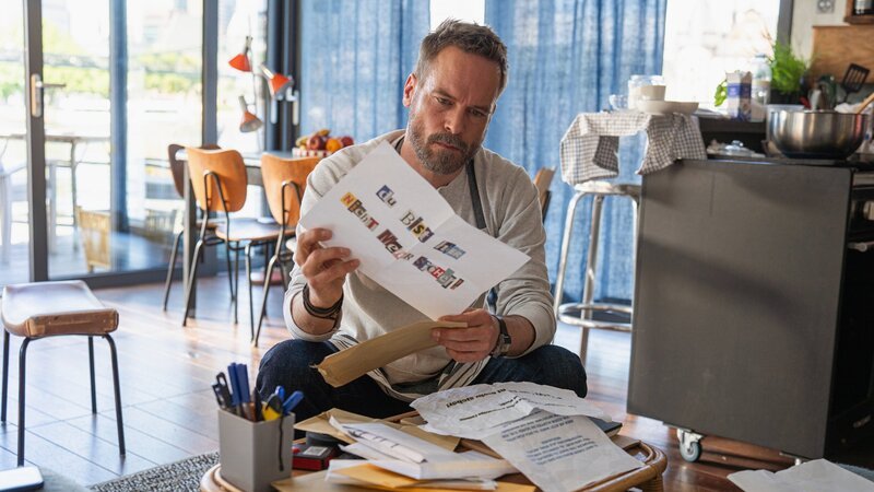Der Privatdetektiv sichtet einen Stapel mit Drohbriefen: Wanja Mues als Leo Oswald – Bild: SRG SSR/​ZDF/​Daniel Dornhöfer