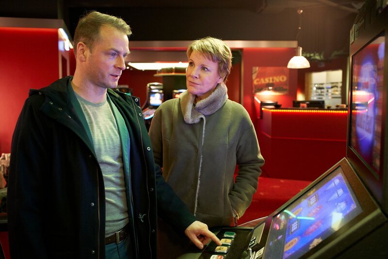 Die Kommissare Jürgen Simmel (Hinnerk Schönemann) und Marie Brand (Mariele Millowitsch) ermitteln im Spielcasino des Opfers. Marie Brand ist erstaunt über Simmels Faszination an Spielautomaten. – Bild: ZDF und Guido Engels