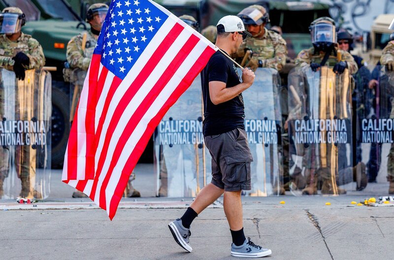 Ein Demonstrant protestiert gegen die Einwanderungspolitik der US-Regierung und passiert Angehörige der Nationalgarde, die am 12. Juni 2025 in Los Angeles hinter dem Bundesgebäude auf Patrouille sind. – Bild: Gina Ferazzi/​Los Angeles Times/​Getty Images