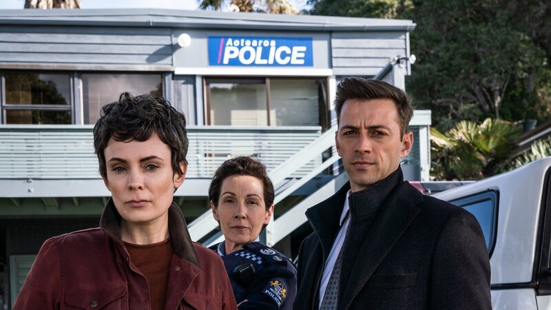 Detective Senior Sergeant Jessica Savage (Kate Elliott, l.), ihr Kollege Detective Sergeant Justin Harding (Ido Drent, r.) und Senior Sergeant Denise Abernethy (Alison Bruce, M.) stehen in Nahaufnahme vor der Polizeistation in Waiheke. In dieser Folge wird die Freundin von Denise bedroht und der Erpresser von Jess wird enttarnt. – Bild: ZDF