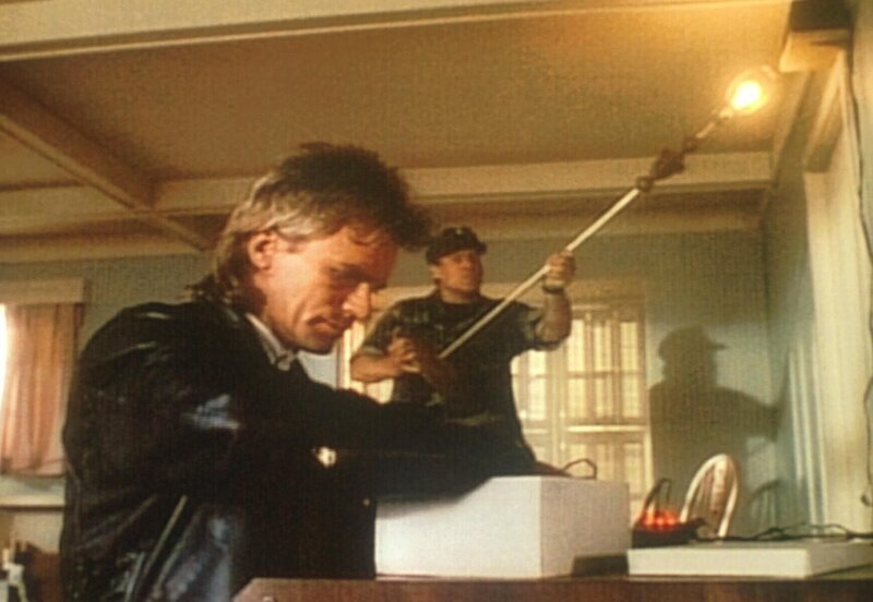 MacGyver (Richard Dean Anderson, l.) und Commander Hilliard (Don Stroud, r.) versuchen, einen Infrarotmelder abzuschalten. – Bild: Paramount Pictures