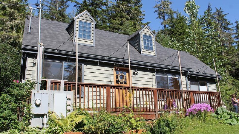 Exterior, house, at Cove House, complete with front porch, grey siding, surrounded by trees, near Juneau, Alaska, as seen on Great American Country’s Living Alaska – Bild: Great American Country/​Scripps Networks, LLC
