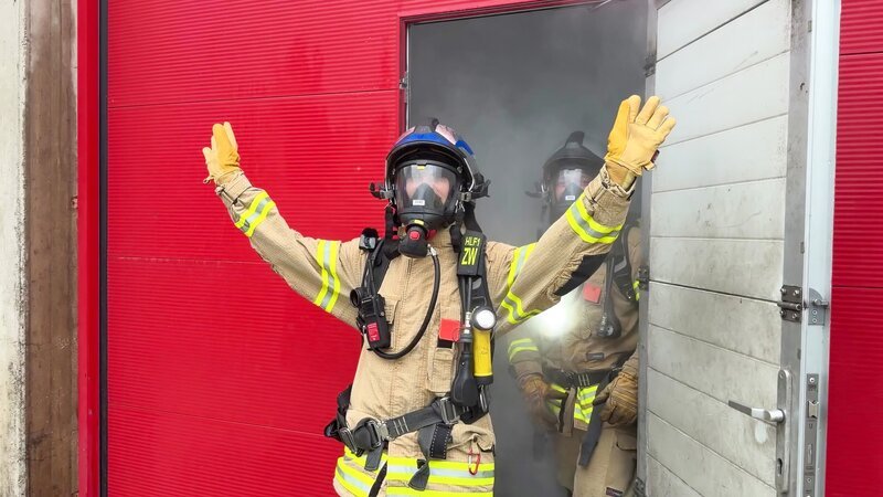 Lena kommt in voller Feuerwehrmontur aus einer verrauchten Halle. – Bild: ORF