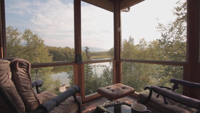 Interior, enclosed patio, at Enchanted Ridge house, chairs facing lake view, near Eagle River, Alaska, as seen on Great American Country’s Living Alaska – Bild: Great American Country/​Scripps Networks, LLC