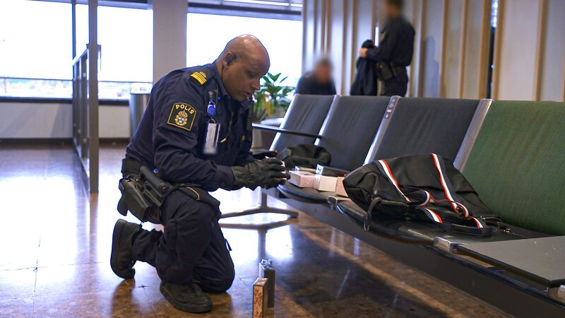 Border policeman Markus looking at stolen items while suspects sits in the background – Bild: Warner Bros. Discovery, Inc. or its subsidiaries and affiliates