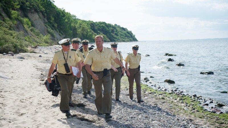 Verdächtige gibt es einige, doch keinen konkreten Beweis. Noch einmal soll der Strand auch im weiteren Umfeld des Tatorts abgesucht werden. Polizist Pöhlmann (Dominic Boeer, 3.v.r.) leitet die Suchaktion. Wird er den entscheidenden Hinweis finden? – Bild: ZDF und Marc Meyerbröker