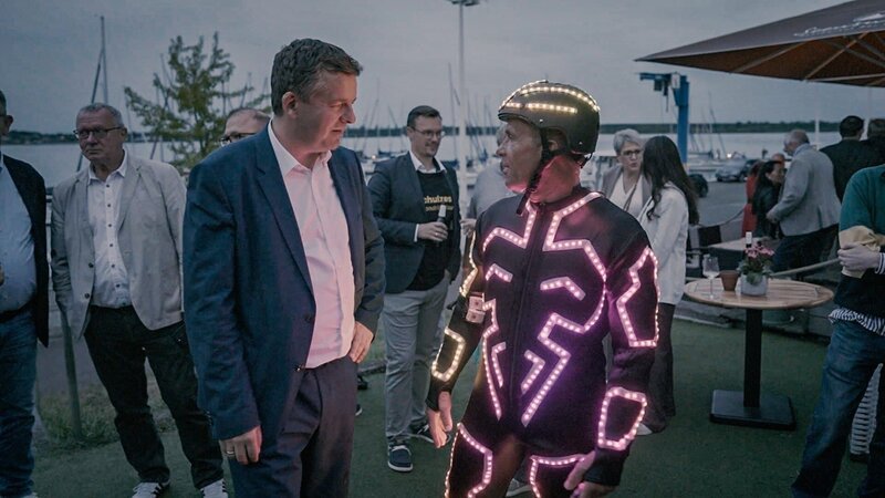 Ministerpräsident Sven Schulze unterhält sich bei einem Parteifest mit einem Akrobaten, der für Stimmung sorgt. – Bild: ZDF