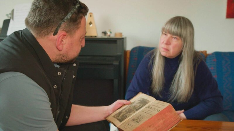 Alex at a client’s home with an old encyclopedia – Bild: Warner Bros. Discovery /​ Philipp Küpper