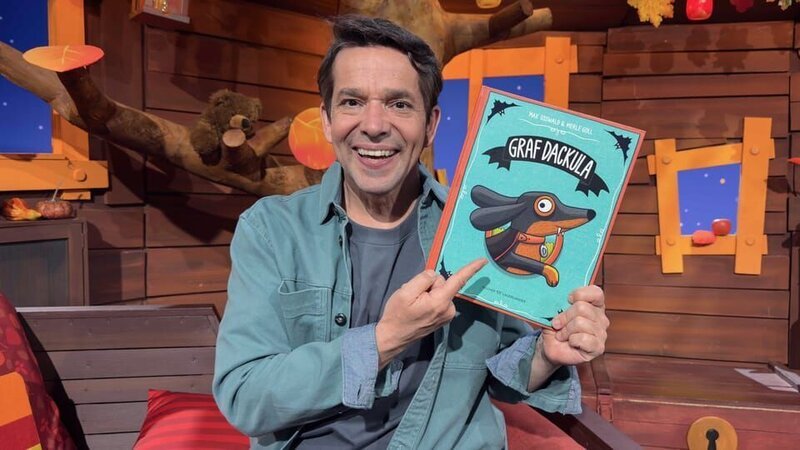 Juri stellt das Buch „Graf Dackula“ vor. Dann erklärt er, was Dackel eigentlich für besondere Hunde sind mit ihren kurzen Beinen und ihrer super Spürnase. – Bild: KiKA