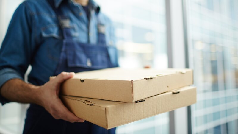Two boxes with fast food being carried by delivery man in uniform for one of clients. – Bild: shironosov /​ Getty Images/​iStockphoto