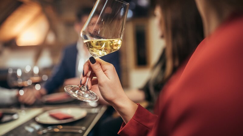 Group of people, men and women, sitting in restaurant together, woman holding wineglass. – Bild: South_agency /​ Getty Images/​iStockphoto