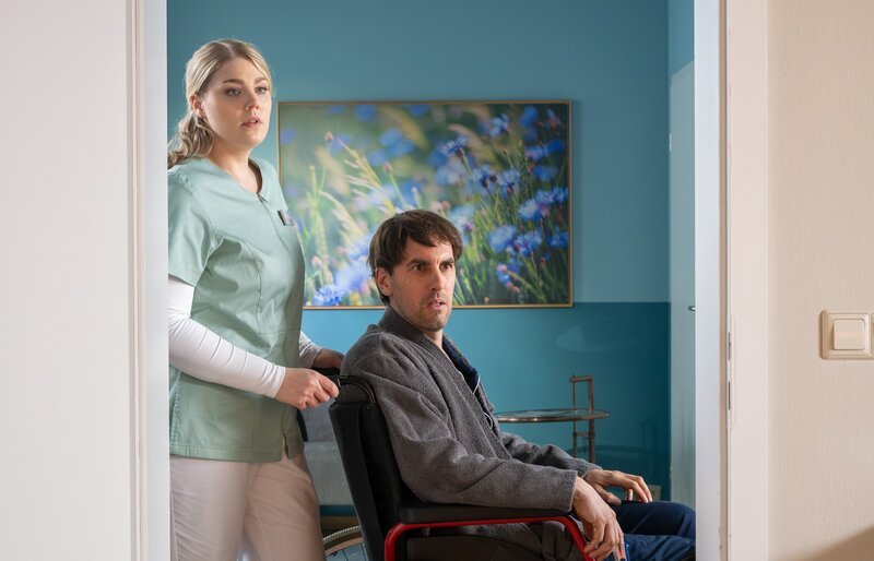 ARD/​MDR „In aller Freundschaft“, Folge 1153, „Des Guten zu viel“. Miriam Schneider (Christina Petersen) will Eike Voss (Jan Hasenfuß) gerade zu einer Untersuchung bringen, als dieser sie bittet, sofort anzuhalten. In einem Behandlungsraum sieht er plötzlich seine Schwiegermutter. – Bild: MDR/​Saxonia Media/​Sebastian Kiss