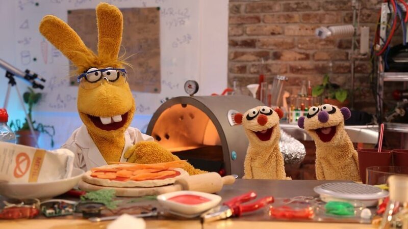 Professorin Hase zeigt den Erdmännchen, wie man Muskelkater mit einem Pizzaofen loswird. – Bild: NDR/​bigSmile