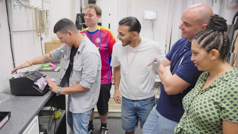 Team Karlsruhe in front of a new money-counting machine – Bild: Warner Bros. Discovery /​ Philipp Küpper