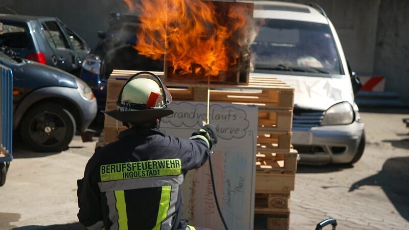 Marco Buhn intending to extinguish a burning model of a room during a practice in the fire station’s yard. – Bild: Warner Bros. Discovery /​ Editorial Team Janus