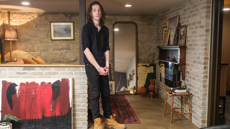 As seen on HGTV’s We Bought a Funeral Home, Rafferty poses in his bedroom makeover, inspired by gothic design and New York City. – Bild: Warner Bros. Discovery /​ Darren Goldstein