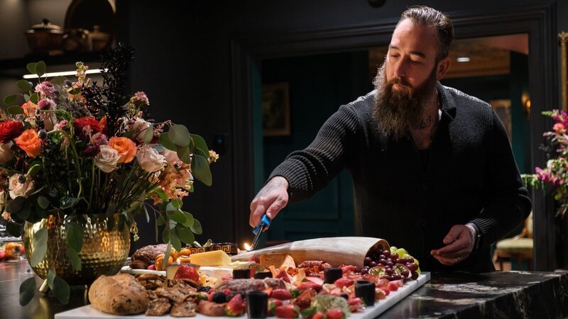 Homeowner Arryn, puts the finishing touches on a charcuterie board in his newly renovated gothic style kitchen, as seen on HGTV’s We Bought a Funeral Home. – Bild: Warner Bros. Discovery /​ Darren Goldstein