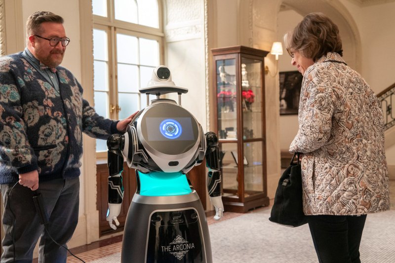 Ein Roboter steht zwischen Howard (Michael Cyril Creighton) und Meckertante Uma Heller (Jackie Hoffman) – Bild: Patrick Harbron /​ Disney