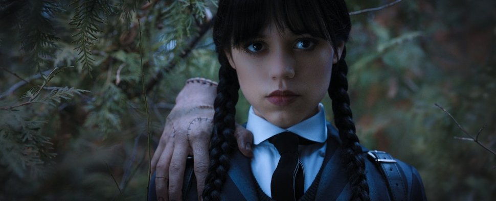 Das eiskalte Händchen lässig auf der Schulter: Wednesday (Jenna Ortega) ermittelt im Wald. – Bild: Netflix