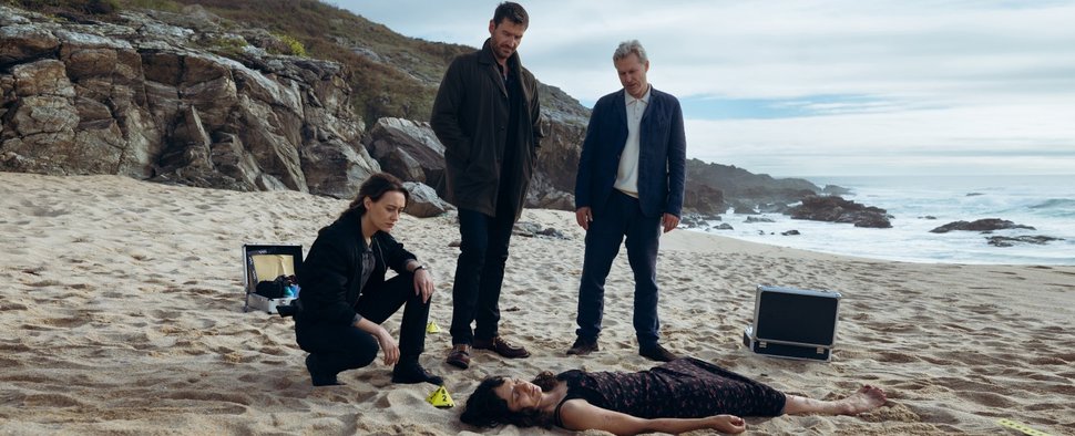 Frauenleiche an der Atlantikküste: Mercédes Navarro (Mercedes Müller, l.), David Acosta (Michael Epp) und Adrían Martinéz (Dirk Borchardt, r.) schauen sich die tote Sofía Serrano (Sylvana Seddig, u.) genauer an. – Bild: ARD Degeto Film/La Diapo Fotografía