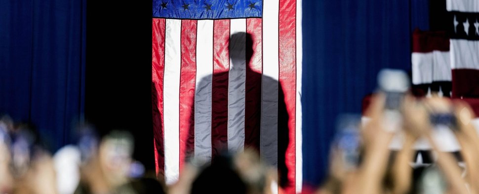 Donald Trumps Schatten hinter der amerikanischen Flagge, als er sich auf seinen Auftritt bei einer „Keep America Great“-Kundgebung im Santa Ana Star Center vorbereitet, Rio Rancho, USA, 2019 – Bild: rbb/IMAGO/ZUMA Press Wire