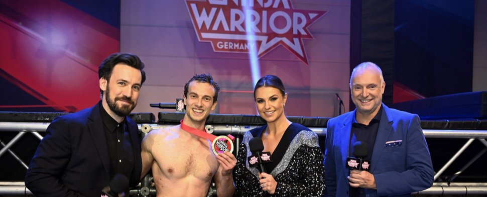 Die „Ninja Warrior Germany“-Moderatoren Jan Köppen (l.), Laura Wontorra und Frank Buschmann (r.) gratulieren dem Sieger Alexander Wurm, der zum dritten Mal in Folge „Last Man Standing“ wurde. – Bild: TVNOW/Markus Hertrich